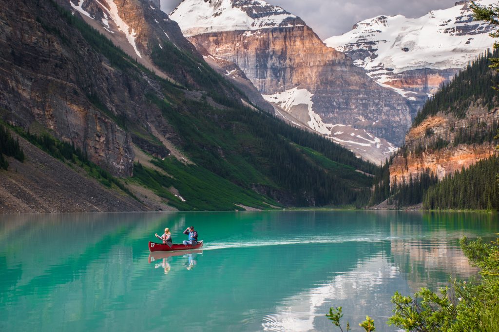 Red canoe floating in turquoise water at Lake Louise. Couple canoeing together in the beautiful glacial Lake Louise at sunrise