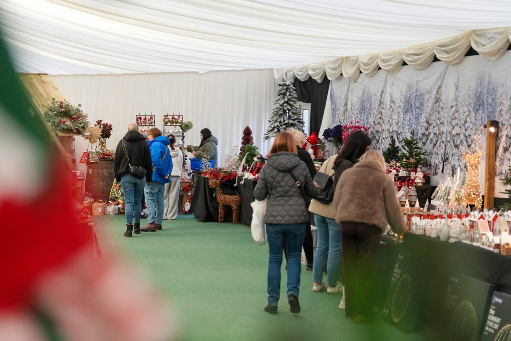 Shoppers browsing winter accessories and handmade gifts beneath festive lighting at Brocksbushes Christmas Fayre.